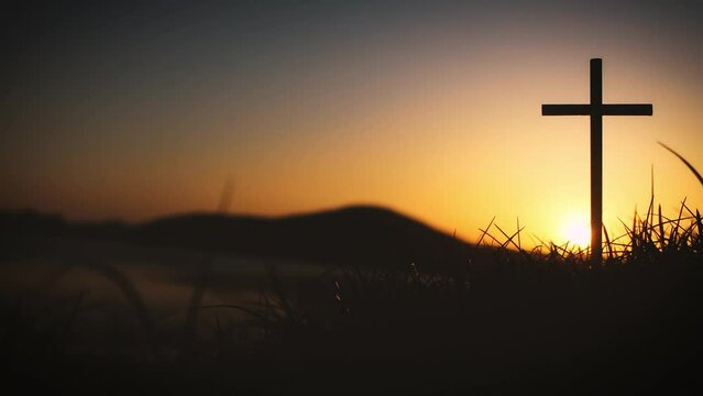 The holy cross of Jesus Christ on the grass with the strong light of the sunset sky symbolizes death and resurrection love.
