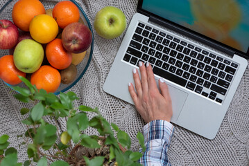 A woman works on a laptop and eats healthy food. Flat layout. Top view of desktop