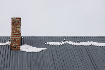 a brick chimney on a metal roof in the winter under the snow. construction concept