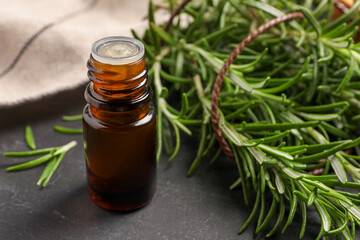 Bottle of essential oil and fresh rosemary on black table, closeup