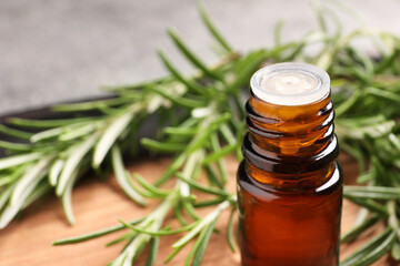 Bottle of essential oil and fresh rosemary on board, closeup. Space for text