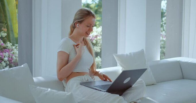 Smiling woman talk to friend on laptop online video call application, sitting on sofa at home. Pleasant conversation millennial woman talking via laptop computer virtual meeting video call at home