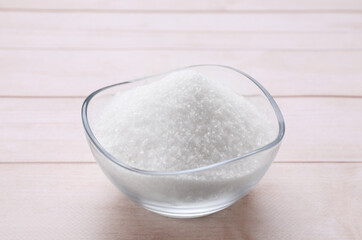 Granulated white sugar in bowl on wooden table, closeup