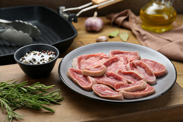 Raw beef tongue pieces, spices and rosemary on wooden board