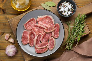 Raw beef tongue pieces and spices on wooden table, flat lay