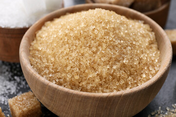 Brown granulated sugar in wooden bowl on black table, closeup