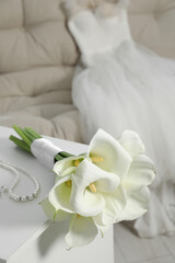 Fototapeta na wymiar Beautiful calla lily flowers tied with ribbon and jewelry on white chest of drawers indoors