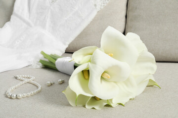 Beautiful calla lily flowers tied with ribbon, wedding dress and jewelry on sofa