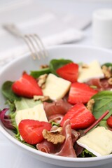 Tasty salad with brie cheese, prosciutto, strawberries and walnuts on table, closeup