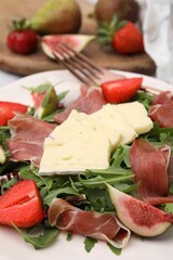 Tasty salad with brie cheese, prosciutto, strawberries and figs on white plate, closeup