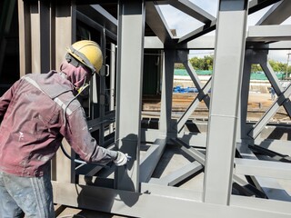 Painters are painting topcoat on the side of the steel beam to achieve the desired thickness.