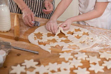 Family in kitchen. Grandmother granddaughter child hands cutting cookies of dough on kitchen table together. Grandma teaching kid girl cook bake cookies. Household teamwork helping family generations