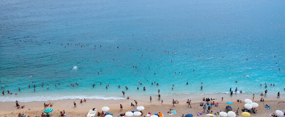 Fototapeta na wymiar Aerial view people relaxing on the beach. Sandy beach with colorful umbrellas, people swimming in the sea bay with clear blue water.