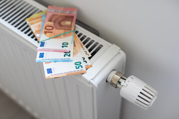 Rising cost of heating and electricity in Europe. Heating radiator with thermostat on which euros lie. Rising energy prices. Energy crisis and recession. 2 euro coins and 100 euro banknotes