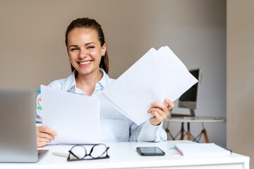 Happy young woman accountant smiling while working with financial documents in the office.