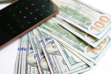 A stack of one hundred dollar bills and a calculator on a smartphone. A stack of one hundred dollar...