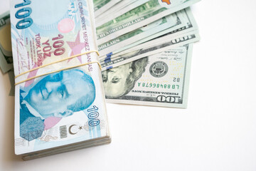 A pack of 100 Turkish lira bills, a pack of 100 dollar bills. A stack of 100 Turkish lira bills, a pack of 100 dollar bills on a light background.