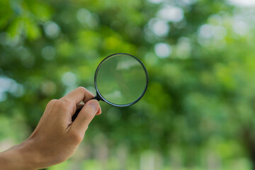 Search and business concept.Hand holding magniflying glass on a natural background.