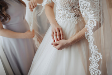 Portrait. Cropped photo. A brunette bride in a dress stands next to her friends. Photo of a ring on the bride's hand. Voluminous veil. Wedding photo. Beautiful bride