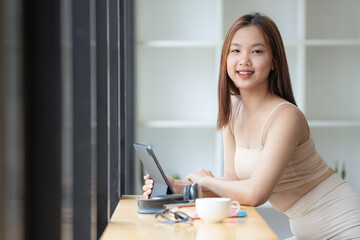 An attractive young Asian female relaxes on her chair in the minimal living room while using a digital tablet.