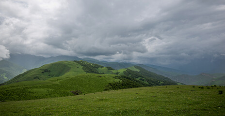 Summer mountain landscape. Amazing view of the valley and lush green pastures in the Caucasus, Georgia. Surrounded by high mountain ranges. Cloudy and rainy day in spring, low storm clouds.