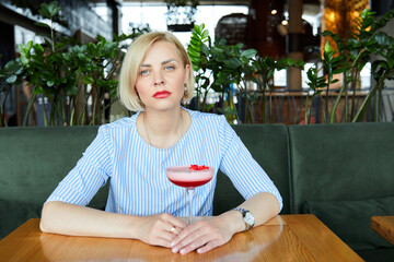 Portrait of attractive young woman drinking coctail in cafe indoor. Beautiful blonde woman relaxing at the bar and drinking a cocktail