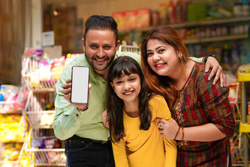 Happy family showing empty smartphone Screen at grocery shop.