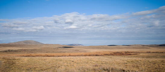 Savanna covered with dry yellow grass and hills on the distant. White clouds in the blue sky....