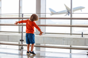 Young child watches a plane take off from an airport window