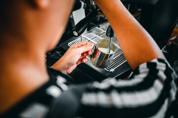 Hand of a barista in the coffee shop preparing and using a coffee machine to steam milk for a coffee menu.