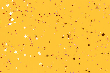 Shiny gold colored stars and crystals confetti on a yellow background. Festive composition. Selective focus.