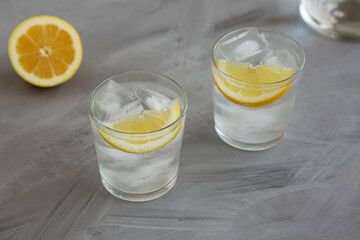 Refreshing Cold Water with Lemon in Glasses on gray background, side view.