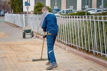 Worker with stiff brush grout and point paving slabs, paving industry. Worker fill the gaps with...
