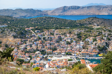 Fototapeta na wymiar High and Breathtaking View of Colorful Houses and Port of Symi Below, the Blue Aegean Sea and the Mountains Beyond