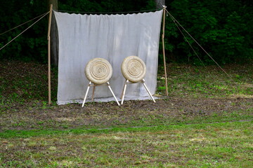 A view of a temporary shooting range prepared for an archery and crossbow competition with targets made out of rolled hay on wooden stands with the background being a cloth hanging from two sticks
