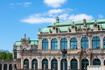 Fototapeta na wymiar Facade of ancient building with beige walls, statues, decorative elements, semicircular windows and green roof. Historical architecture in the baroque style. Dresden, Art Gallery, Germany, May 2023 