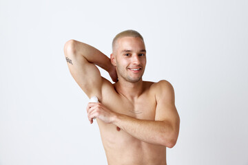 Portrait of handsome young man with well-kept skin, posing shirtless, using deodorant against white studio background. Concept of men's beauty, skincare, cosmetology, spa, health. Copy space for ad