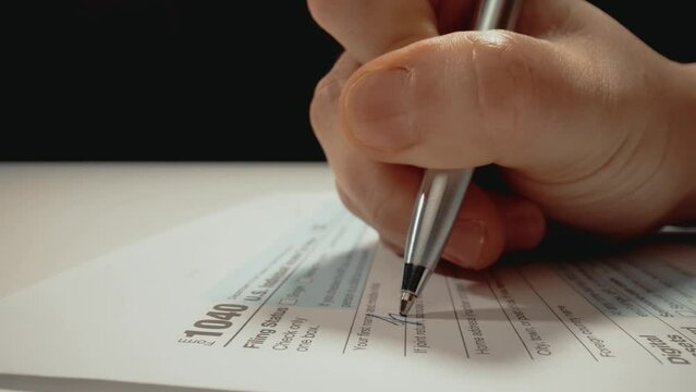 Closeup macro shot movement shot of corporate accountant or individual tax payer filling out 1040 tax form with name and personal information preparing for tax season and submitting financial report.