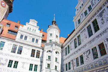 Obraz premium View of ancient building with white walls and grey graphic paintings, with towers and spires, windows and red roof. Old architecture, palace. Sunny day with blue sky. Dresden, Germany, May 2023.
