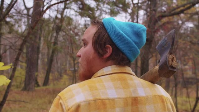 Woodcutter walk on forest with axe on shoulder