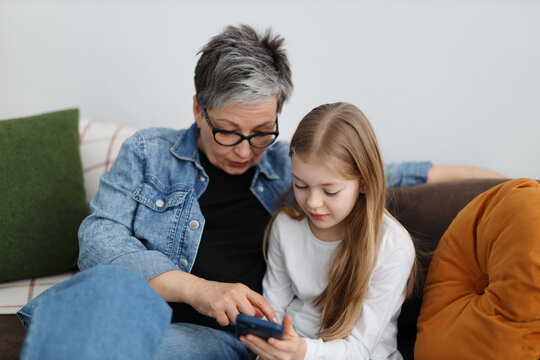 A cute girl with grandmother spending time together while watching videos or photos on mobile phone.