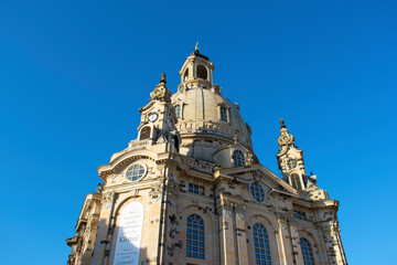 Fototapeta na wymiar View of an old church with beige stone walls, dome, long semicircular windows and decorative elements on the facade. Frauenkirche. Old architecture. Sunny day with blue sky. Dresden, Germany, May 2023