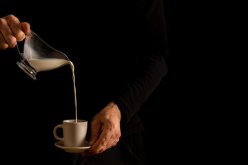Fototapeta na wymiar the hands of an unrecognizable man in the shadows pouring milk from a glass carafe into a coffee cup