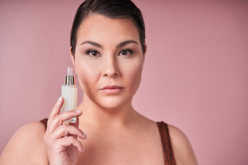 Asian lady carrying essential oil for facial skin and looking camera