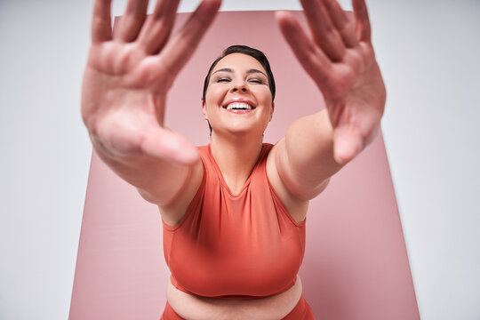 Young Caucasian Plus Size Female Model Stretching On Pink Background