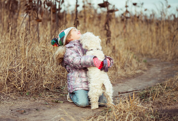 little cute girl with her dog breed White Terrier walking in a field