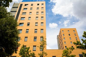 Bottom-up view of the facade of a yellow orange tall apartment building in a residential neighborhood. Renting, buying, investing in real estate. Modern city architecture in sunny day. Madrid, Spain.