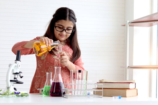 Cute Indian school girl in India traditional dress costume doing science experiments in laboratory, young scientist kid with microscope and lab equipment learning biologics and chemistry in classroom.