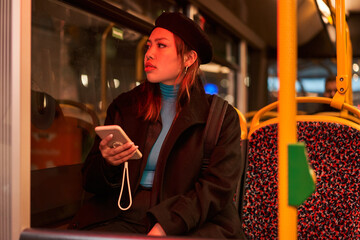 Teen asian woman in black hat messaging on smartphone at the bus