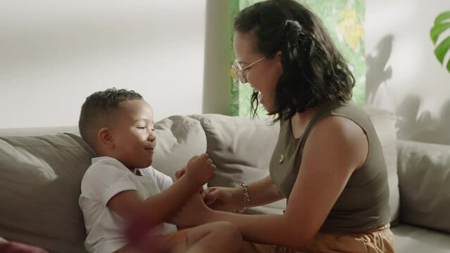 Adorable little kid son playing patty cake with latina mom at home. Happy mixed race family mother and cute little boy son learning funny game having fun enjoying sweet moments together.
